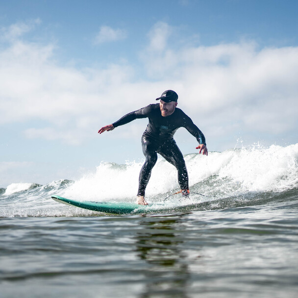 Surfer mit Sonnenhut reitet konzentriert eine Welle Richtung Ufer