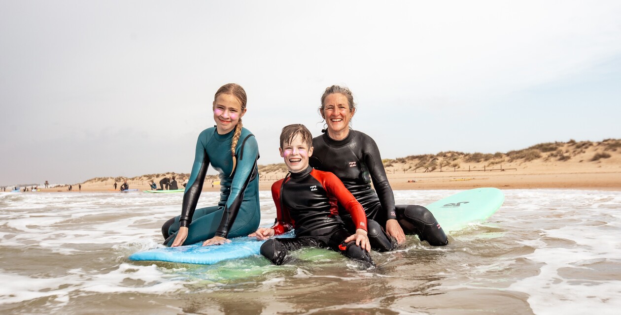Mutter und Kinder auf Surfbrett lächeln im flachen Wasser