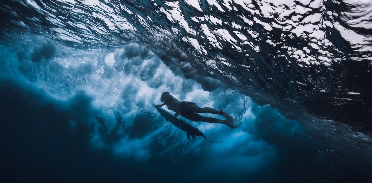 Surfer taucht beim Duck Dive unter eine brechende Welle
