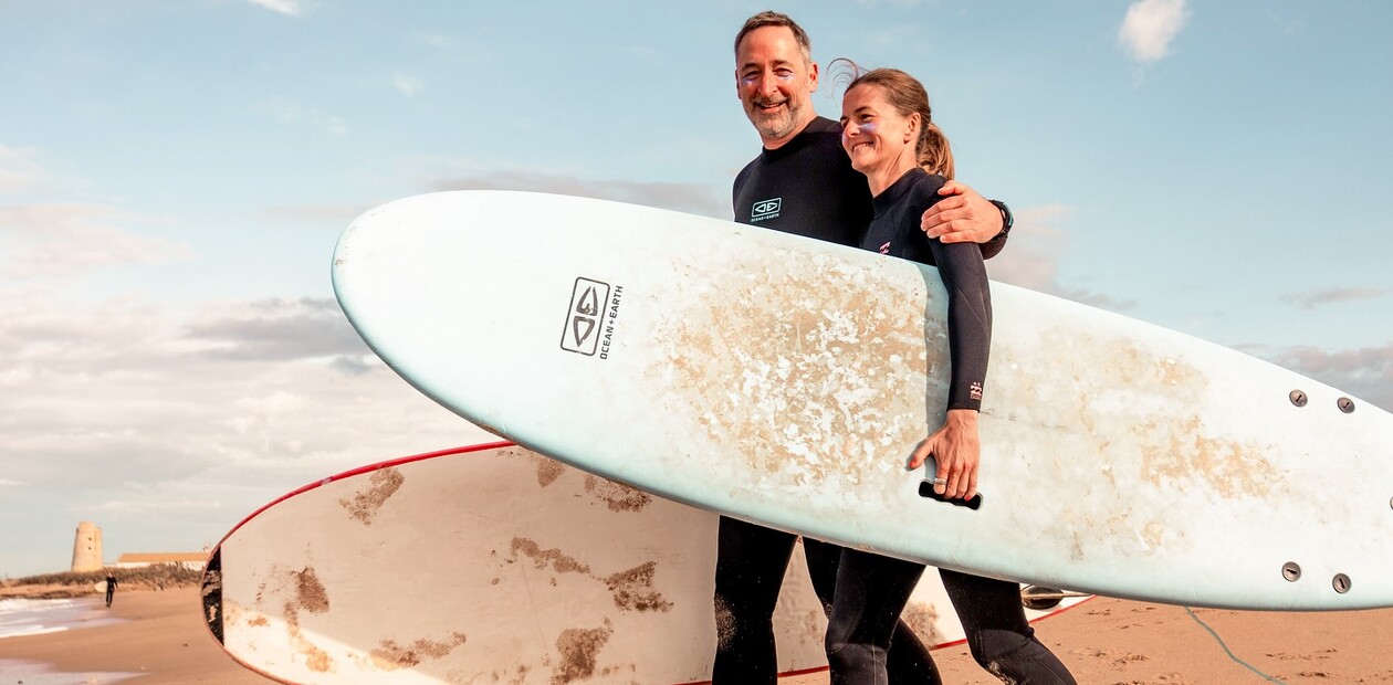 Ehemann legt den Arm um seine Frau am Strand mit Surfbrettern