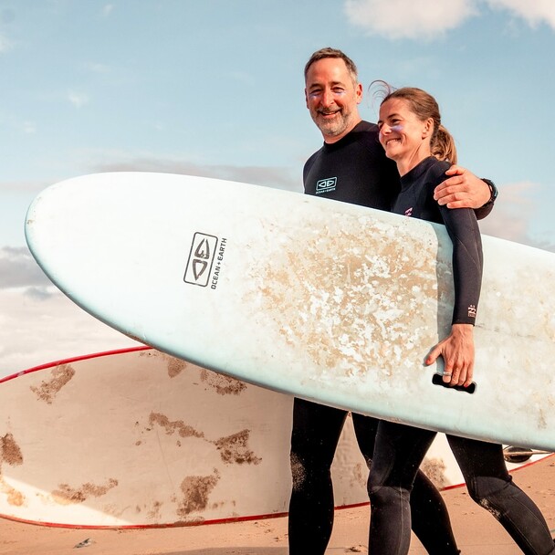 Ehepaar in Neoprenanzügen mit Surfbrettern am Strand