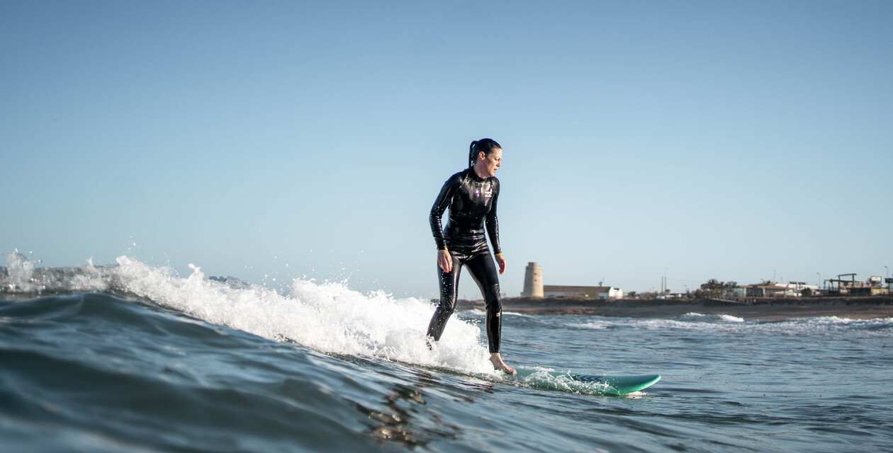 Surferin auf Welle mit Torre von El Palmar