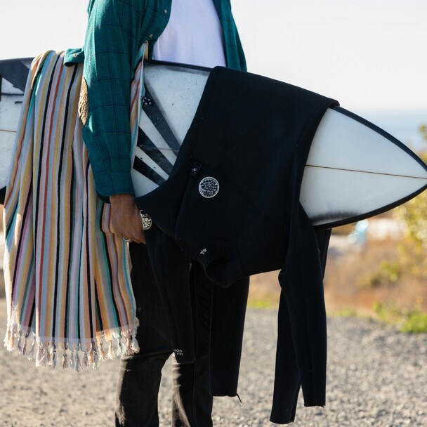 Surfer mit Neoprenanzug und Handtuch über dem Board geht zum Strand