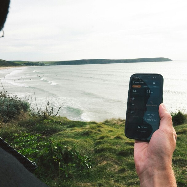 Handy mit geöffneter Surf-Vorhersage-App vor Strandkulisse