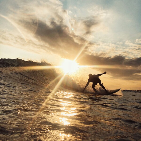 Silhouettierter Surfer reitet mit Sonne im Rücken in Richtung Kamera