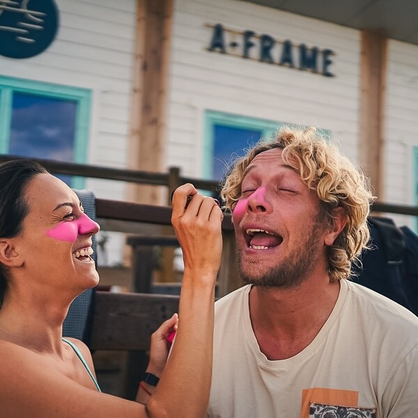 Weiblicher Gast trägt einer anderen Person pinkes Zink im Surfcamp auf