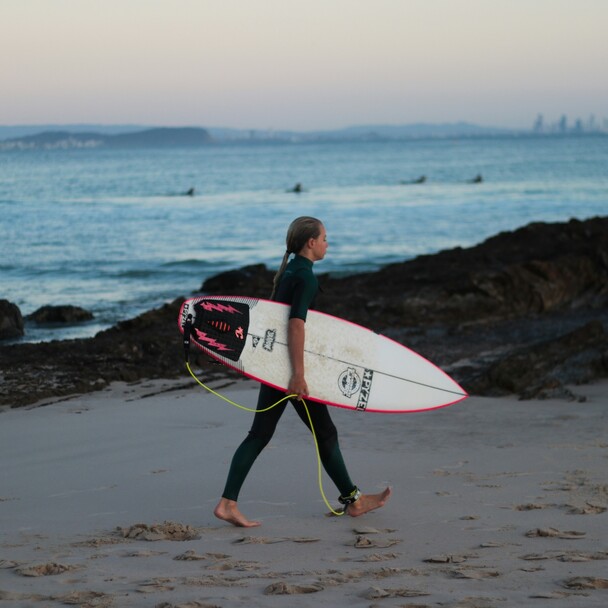 Junges Kind im Neoprenanzug geht morgens mit Surfbrett