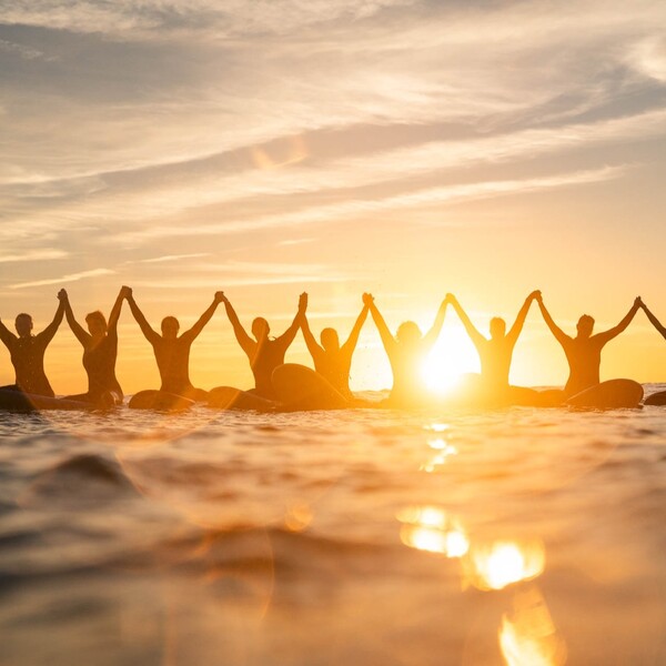 Surfer mit erhobenen Händen bei Sonnenuntergang