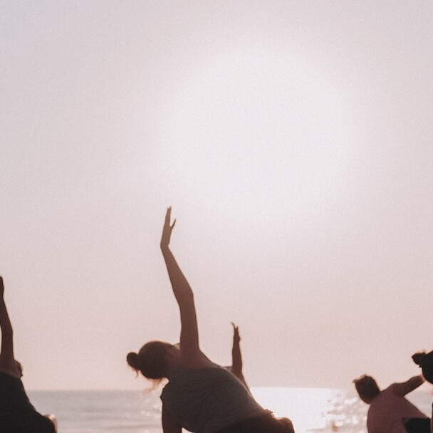 Gruppe macht Yoga am Strand unter rosa Morgenhimmel