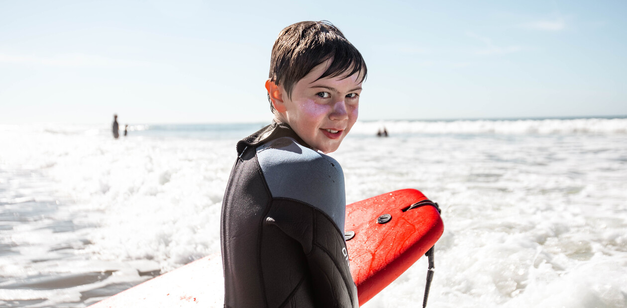 Junger Junge hält ein rotes Soft-Top-Surfbrett