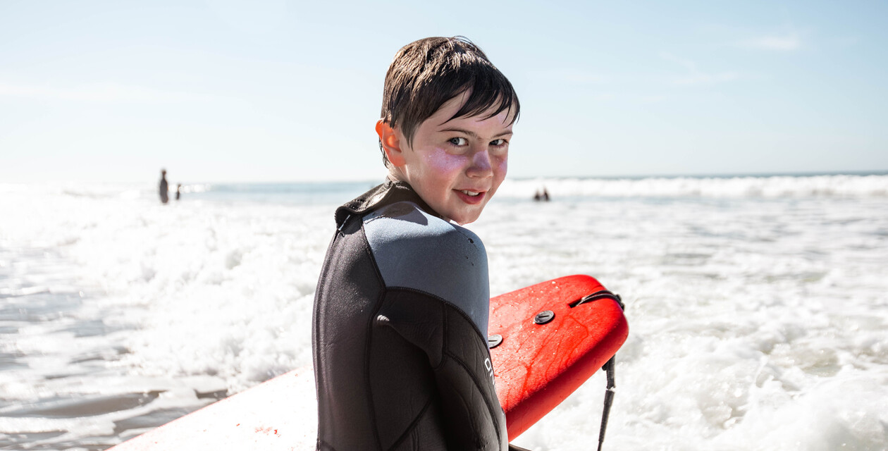 Junger Junge mit rotem Soft-Top-Surfbrett, schaut in die Kamera