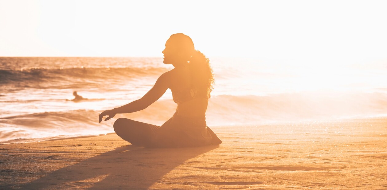 Frau sitzt bei Sonnenuntergang am Strand mit heruntergezogenem Neoprenanzug