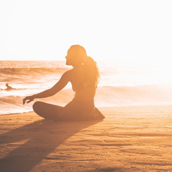 Frau sitzt bei Sonnenuntergang am Strand mit heruntergezogenem Neoprenanzug