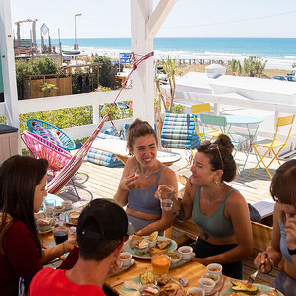 Surfcamp Spanien, Gruppe von Frauen frühstückt auf der Terrasse, Meer im Hintergrund