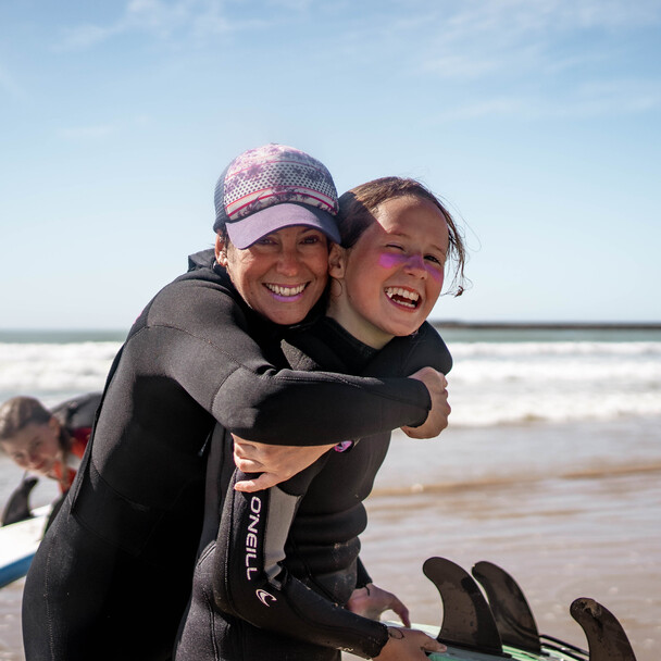Mutter und Tochter lachen am Strand, Surfcamps für Erwachsene