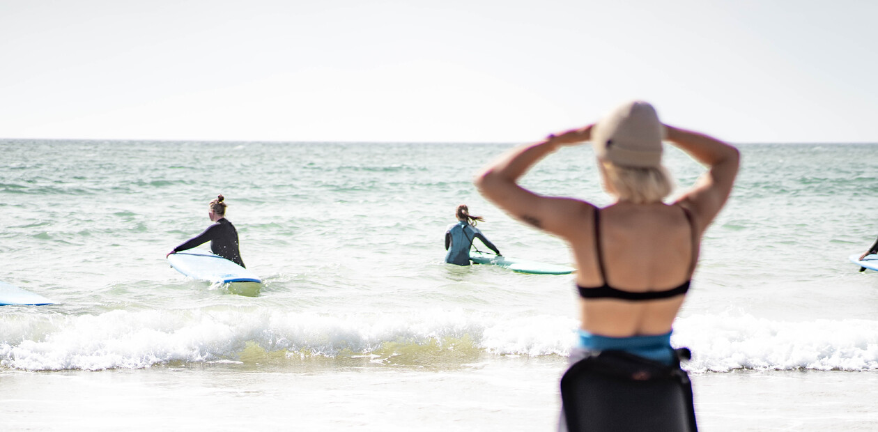 Weibliche Surflehrerin beobachtet Schüler beim Üben im flachen Wasser