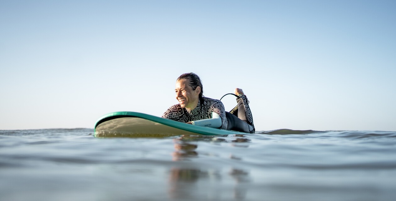 Mädchen liegt im Neoprenanzug auf Soft-Top-Surfbrett und lächelt in der Sonne