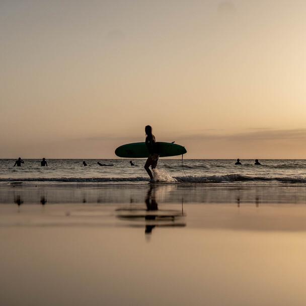 Älterer Surfer geht als Silhouette bei Sonnenuntergang am Strand entlang