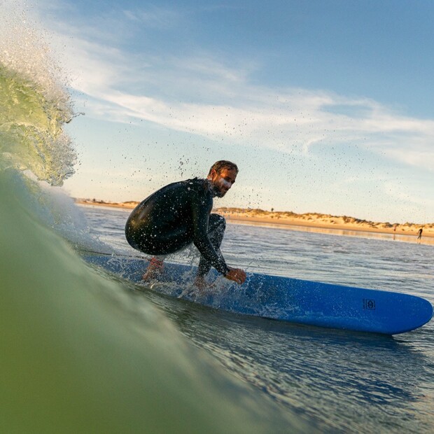 Surfer auf blauem Surfbrett in grüner Welle, Surfkurs