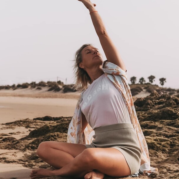 Frau sitzt am Strand in Yoga Pose, Surfkurs