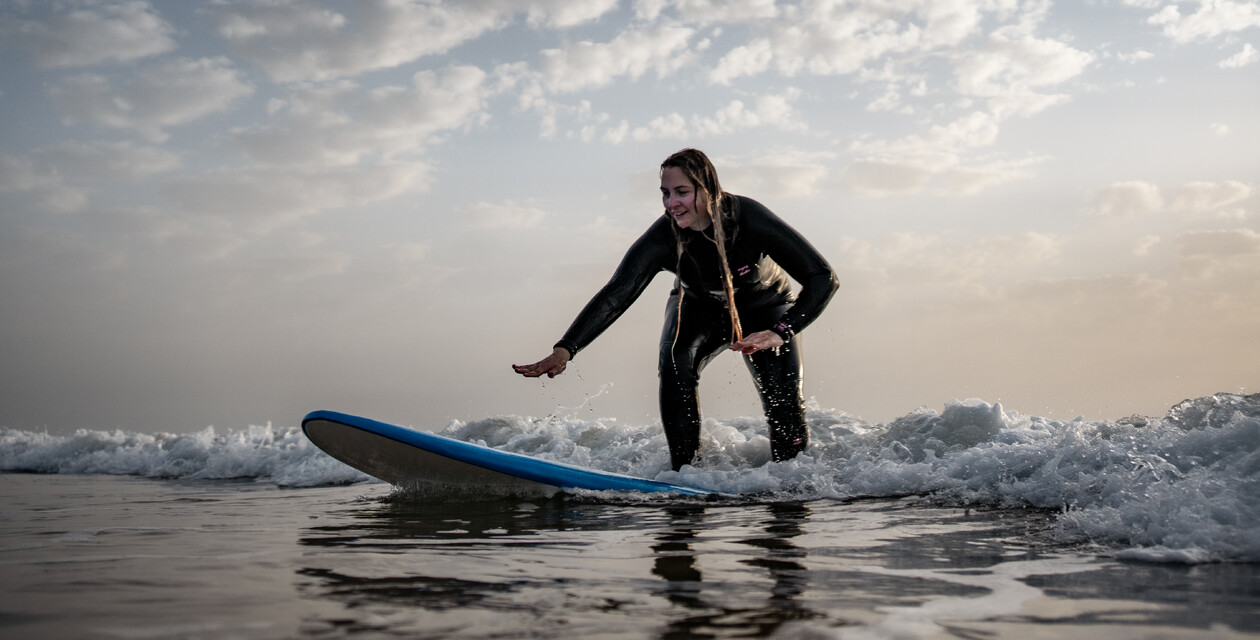 Frau steht auf dem Surfbrett im Weißwasser im Surfkurs für Anfänger