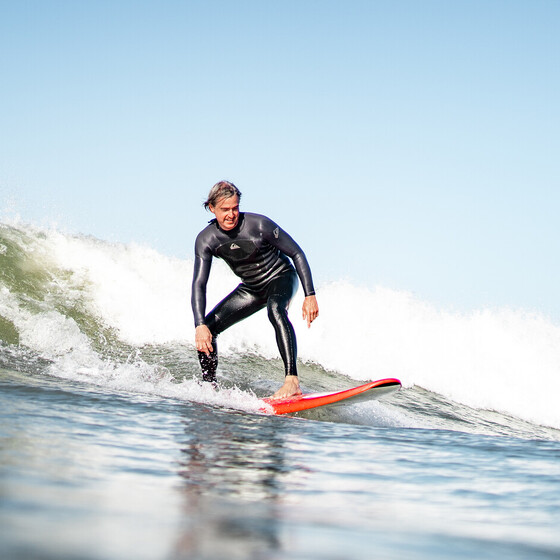 Surfer auf rotem Surfbrett in grüner Welle im Surfkurs