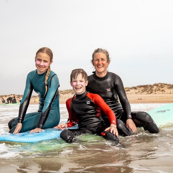 Mutter und zwei Kinder sitzen auf Surfbrettern und lächeln in die Kamera