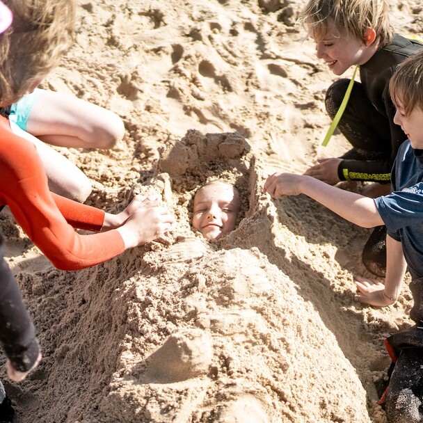 Kinder vergraben ihren Freund im Sand am Strand von El Palmar
