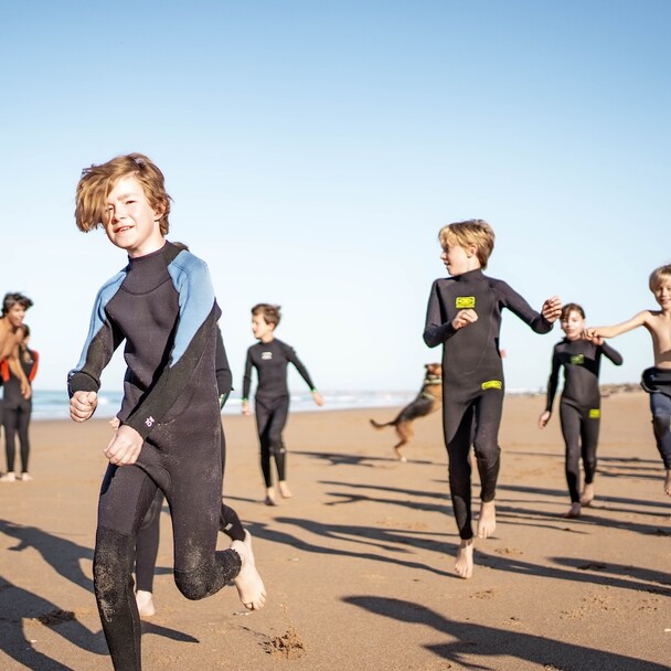 Kinder in Neoprenanzügen rennen lachend am Strand