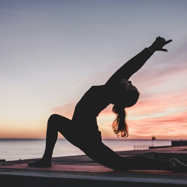 Frau als Silhouette bei Sonnenaufgang bei einer Yoga-Dehnung am Strand