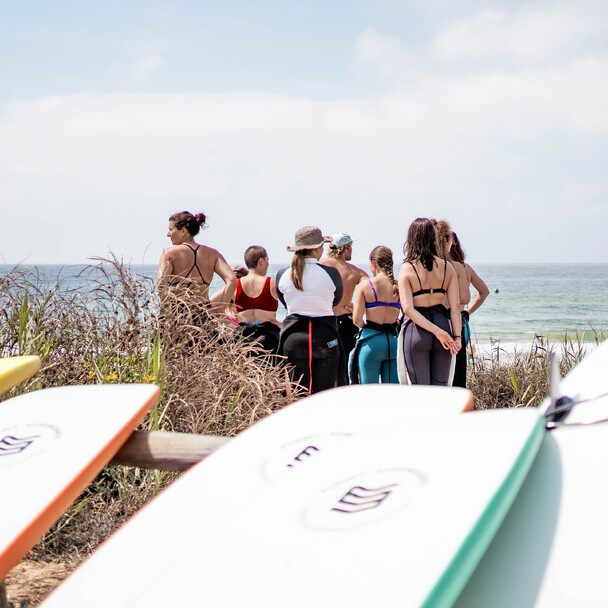 Surfschüler warten am Strand auf den Beginn der Aufwärmübung