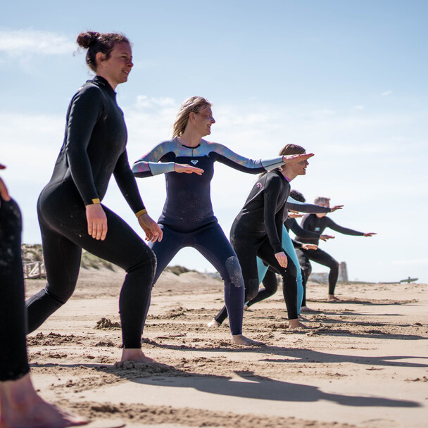 Reihe von Surf-Anfängern im Neoprenanzug beim Training am Strand