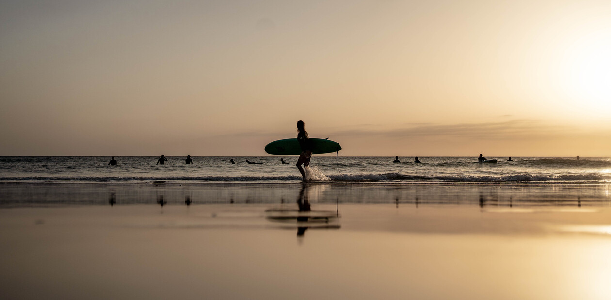 Person mit Surfbrett als Silhouette vor dem Sonnenuntergang