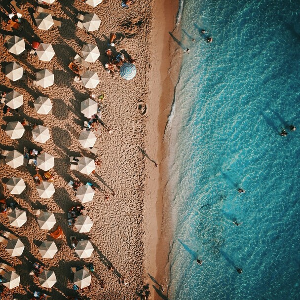 Draufsicht auf Strand mit Ufer, Sonnenschirmen und vielen Menschen
