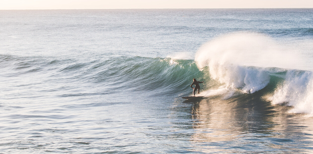 Surfer im Neoprenanzug reitet an einem sonnigen Tag eine kopfhohe Welle