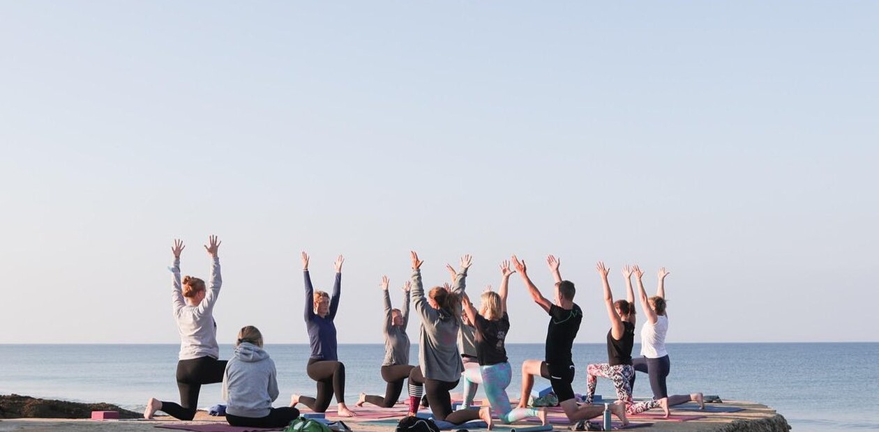 A group of people practice yoga in the early morning light by the ocean at A-Frame Surf & Yoga Camp, enjoying a peaceful start to the day