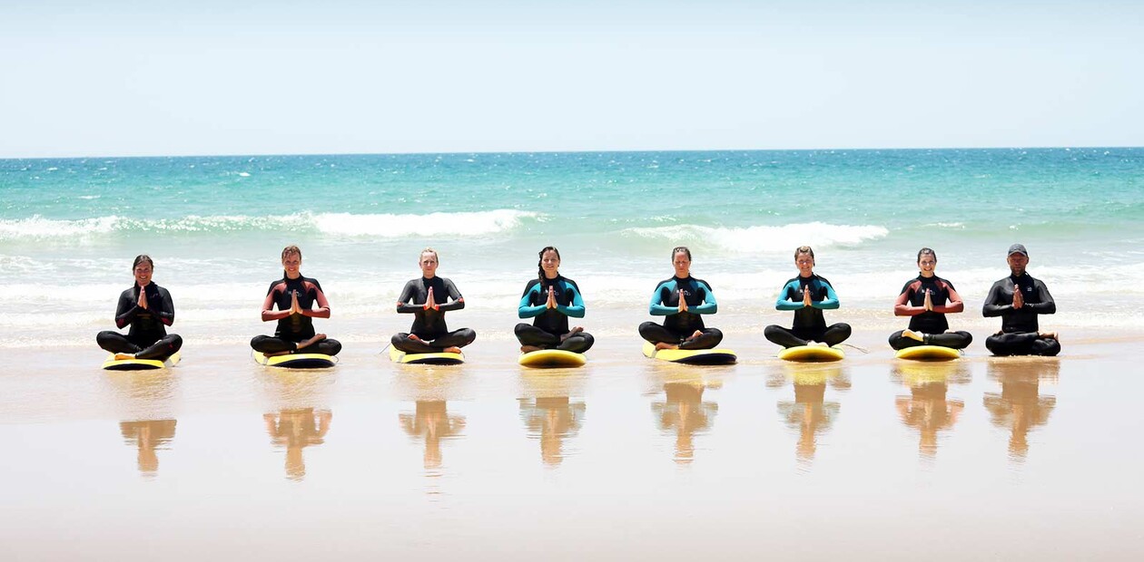 Surf and yoga camp, group does yoga on surfboards on the beach