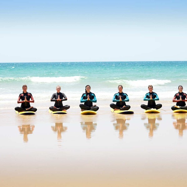 Surf and yoga camp, group does yoga on surfboards on the beach