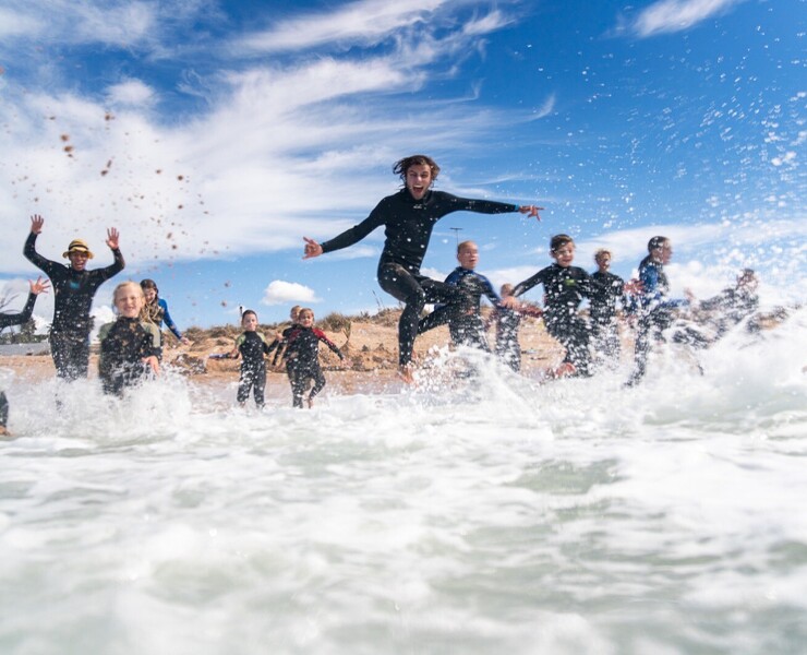 Surf camps for families, children playing in the water in wetsuits