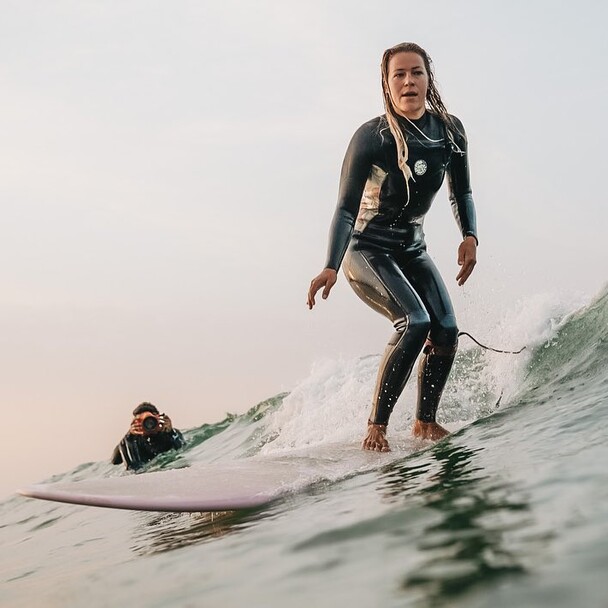 Fotos beim Surfen lernen in Spanien, Frau auf Welle, Hintergrund Fotograf