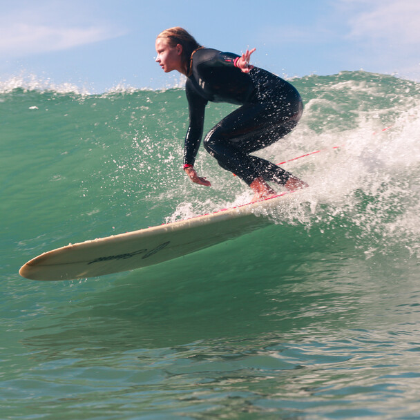 Yoga und Surf Retreat, Surferin reitet Welle mit Longboard ab